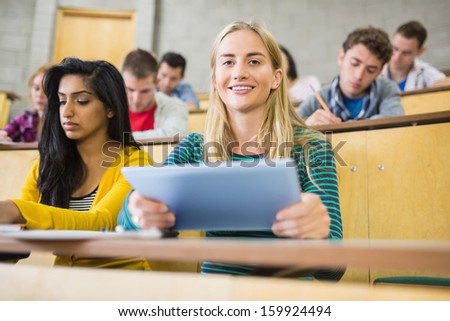 Portrait of a female holding tablet PC with students at the lecture hall
