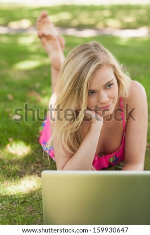 Day dreaming young woman lying in front of her notebook on a lawn