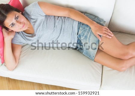 Casual young woman lying on a white couch at home smiling at camera