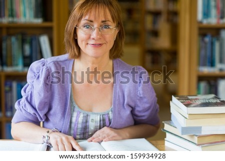 Close-up portrait of a smiling mature female student at desk in the library