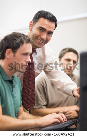 Portrait of smiling teacher showing something on screen to mature student in the computer room