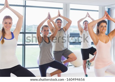 Fitness class and instructor standing in tree pose at  exercise studio