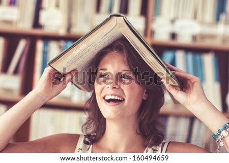 Close-up of a cheerful female student holding book over her head in the library