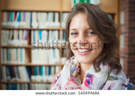 Close-up portrait of a smiling female student against bookshelf in the library