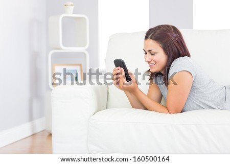 Content casual woman working with her smartphone while lying on her couch in the living room