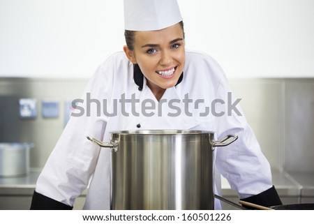 Young smiling chef standing behind saucepan in professional kitchen
