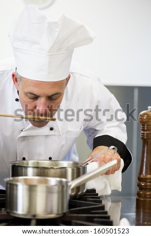 Concentrating head chef tasting sauce with wooden spoon in professional kitchen