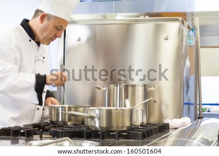 Concentrated head chef stirring in pot in professional kitchen