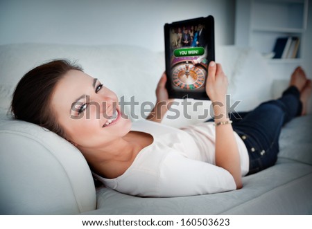 Happy woman lying on couch and gambling on tablet at home in living room