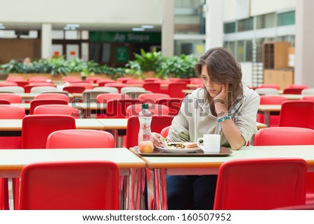 Alone and sad female student sitting in the cafeteria with food tray
