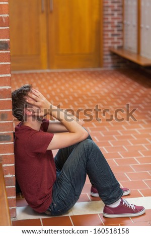 Unhappy handsome student covering his face in school