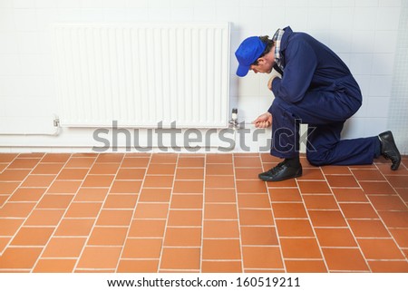 Handyman in blue boiler suit repairing a radiator in bright room