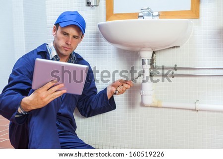Serious plumber consulting tablet in public bathroom