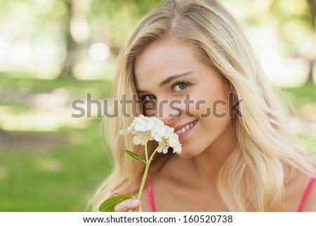 Beautiful blonde woman smelling a flower sitting in a park smiling at camera
