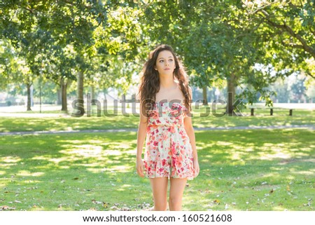 Stylish day dreaming brunette walking on grass in a park on a sunny day