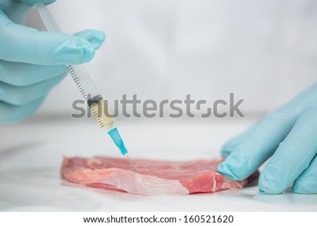 Close-up of gloved researcher\'s hands injecting meat against blurred background
