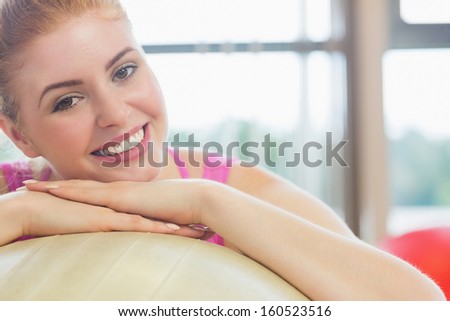 Close-up portrait of a beautiful young woman leaning on exercise ball in fitness studio