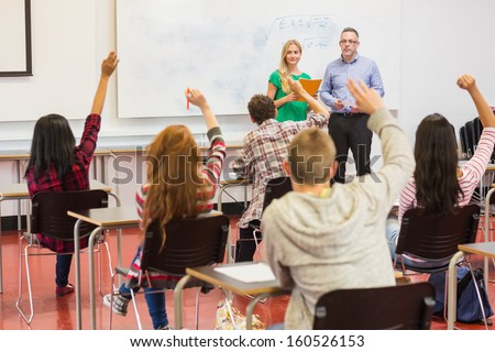 Rear view of students with hands raised in the classroom