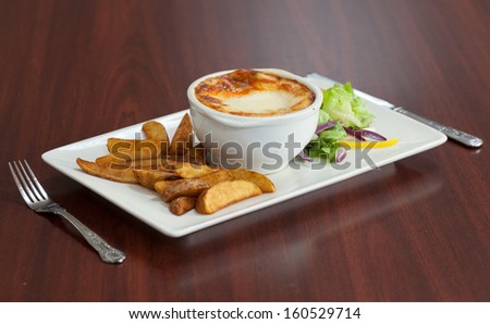 Side view of lasagna with salad and potatoes on wooden table