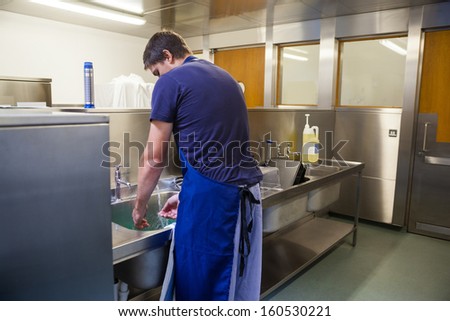 Kitchen porter washing up at sink in professional kitchen