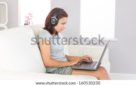 Concentrated casual woman working with her notebook while listening to music and sitting on a couch