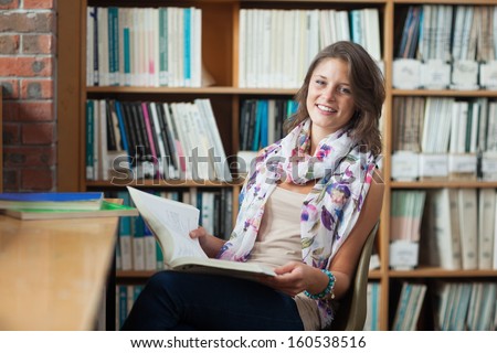 Portrait of a happy female student sitting on chair and with a book in the library