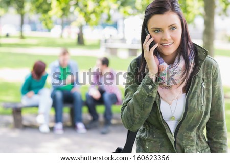 College girl using mobile phone with blurred students sitting in the park