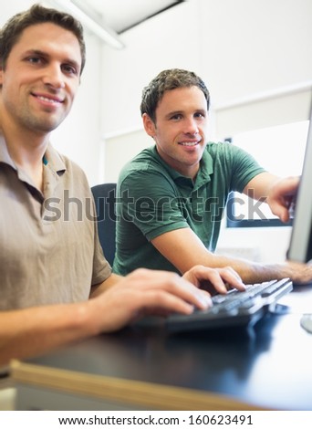 Portrait of smiling teacher showing something on screen to mature student in the computer room