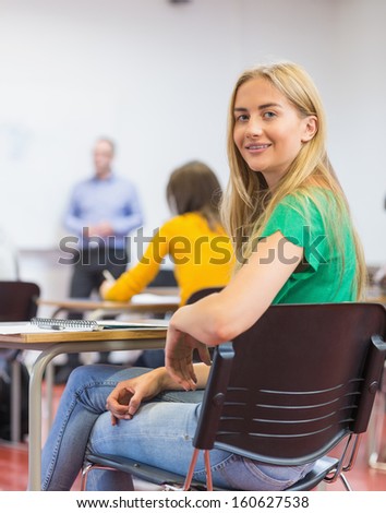 Portrait of a smiling young female student with blurred teachers and others in the classroom