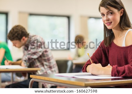 Portrait of a smiling female student with others writing notes in the classroom