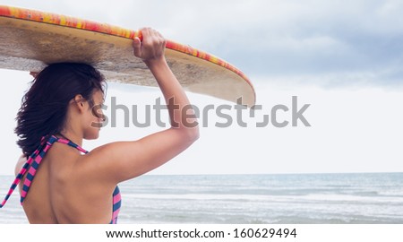 Side view of a young woman carrying surfboard on head at beach