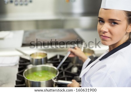 Young happy chef stirring sauce in professional kitchen