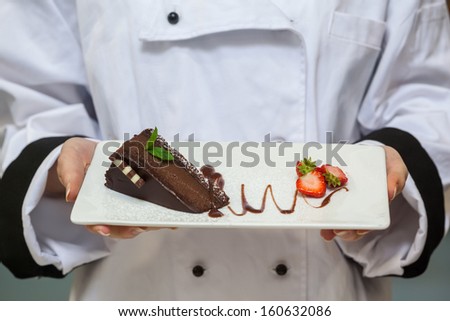 Chef presenting chocolate cake with strawberries on white plate