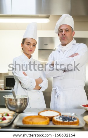 Frowning chef and head chef standing arms crossed in professional kitchen