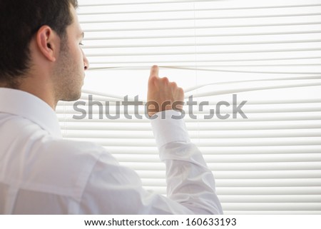 Rear view of handsome businessman spying through roller blind in bright office