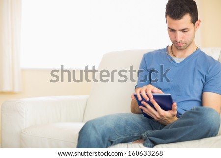 Casual calm man using tablet sitting on couch in bright living room