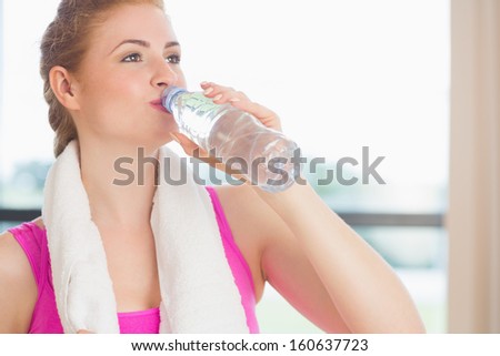 Young woman with towel around neck drinking water in fitness studio