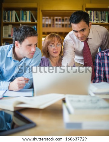 Mature students sitting at the library while looking at teacher use a laptop
