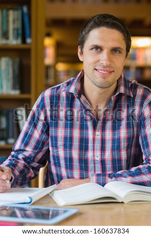 Portrait of a smiling mature male student sitting at desk in the library