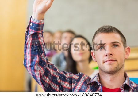 Close-up of a young male student raising hand by others in a row at the classroom