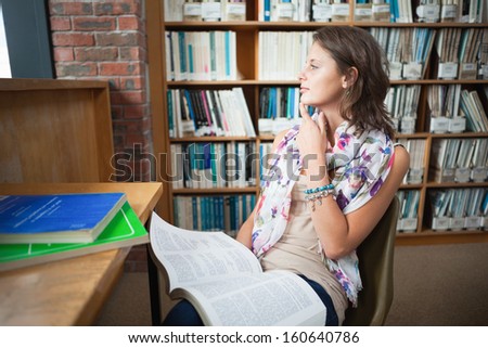 Thoughtful female student sitting on chair with a book in the library