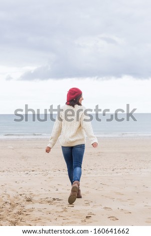 Full length rear view of a young woman in stylish warm clothing walking on beach