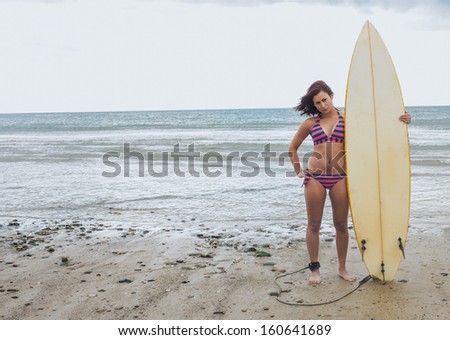 Full length portrait of a young bikini woman holding surfboard at beach