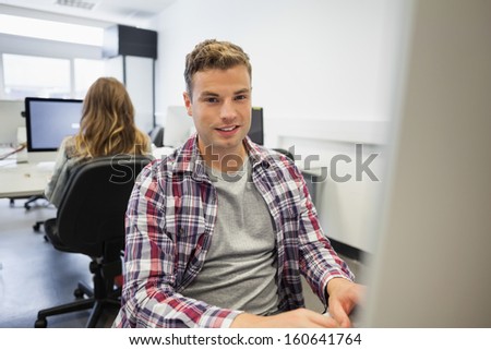 Handsome smiling student working on computer in computer room at college