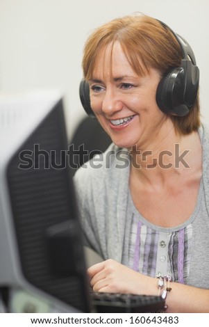 Happy mature woman working on computer while listening to music
