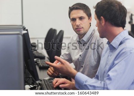 Two attractive men talking in computer class pointing at monitor