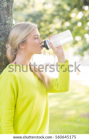 Fit calm blonde drinking from water bottle in a park on a sunny day