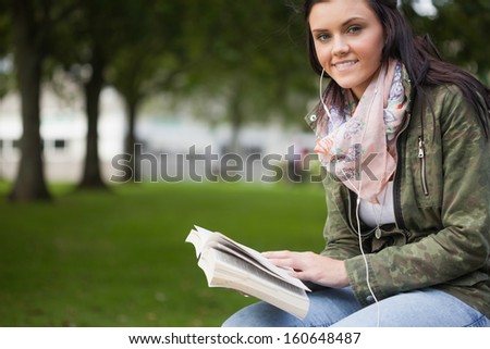 Gleeful brunette student sitting on bench reading on campus at college
