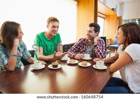Four casual students having a cup of coffee chatting in college canteen