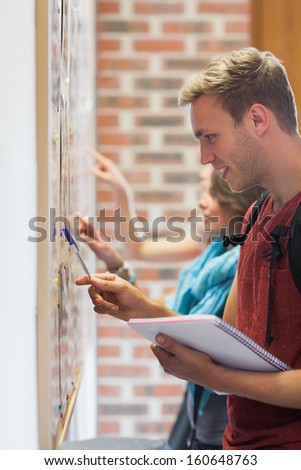 Smiling students searching something on notice board in college